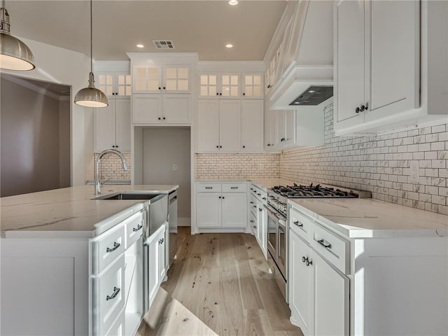 kitchen with light wood finished floors, stainless steel stove, custom range hood, white cabinets, and a sink