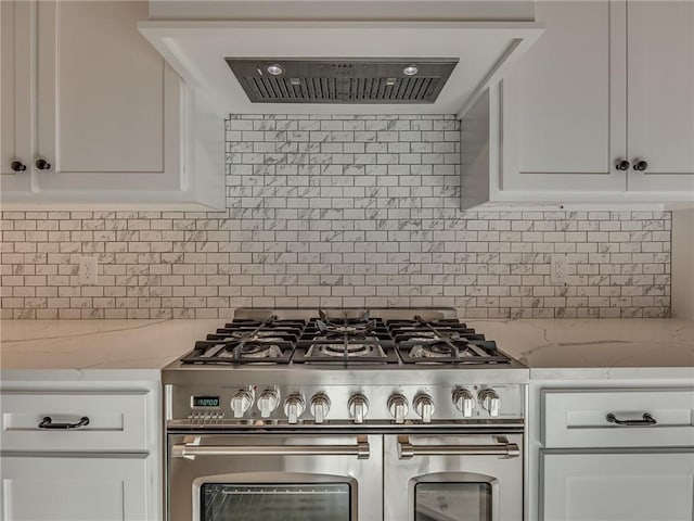 kitchen featuring range with two ovens, ventilation hood, backsplash, and white cabinetry