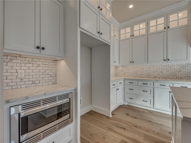 kitchen featuring light wood-style floors, stainless steel microwave, white cabinets, and light stone counters