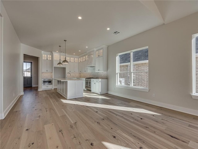 kitchen featuring custom range hood, visible vents, high end stainless steel range oven, decorative backsplash, and a sink