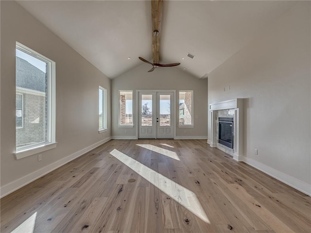 unfurnished living room featuring baseboards, a tile fireplace, light wood-style flooring, vaulted ceiling with beams, and french doors