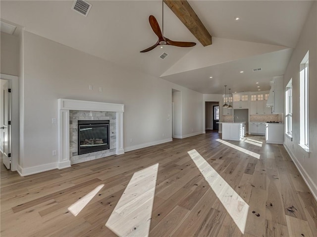 unfurnished living room with visible vents, light wood-style flooring, a stone fireplace, high vaulted ceiling, and beam ceiling