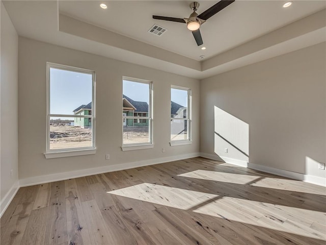 spare room featuring wood-type flooring, a raised ceiling, visible vents, and baseboards