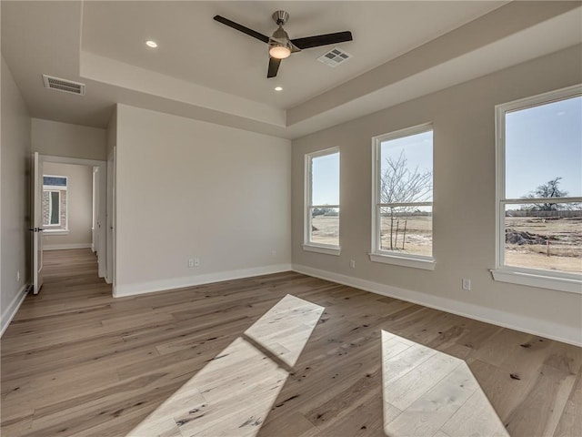 spare room with light wood-type flooring, baseboards, visible vents, and a tray ceiling