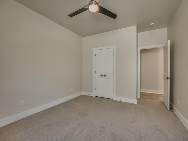 unfurnished bedroom with a closet, baseboards, a ceiling fan, and light colored carpet