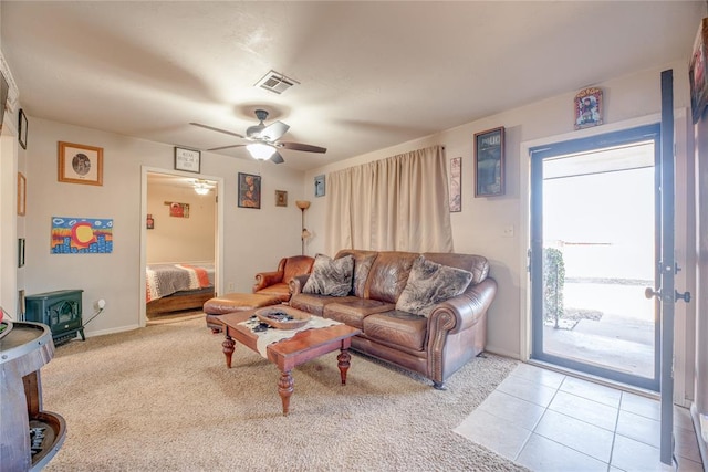 living room featuring a wood stove, visible vents, ceiling fan, and light tile patterned floors