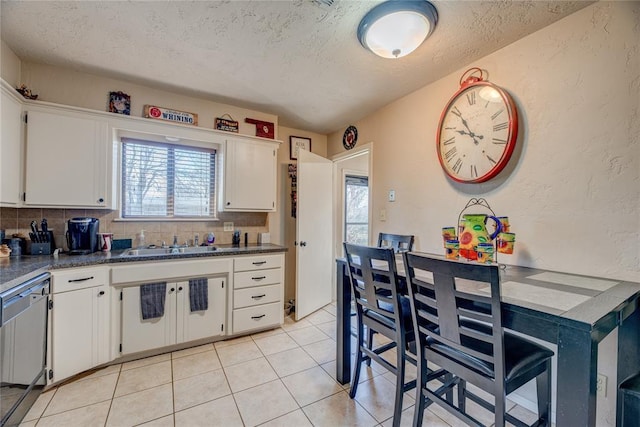 kitchen featuring light tile patterned floors, a sink, white cabinets, backsplash, and dishwasher