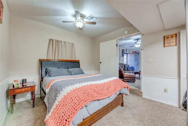 carpeted bedroom with ceiling fan, visible vents, and wainscoting