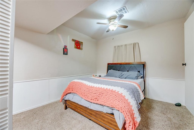 carpeted bedroom with ceiling fan, wainscoting, and visible vents