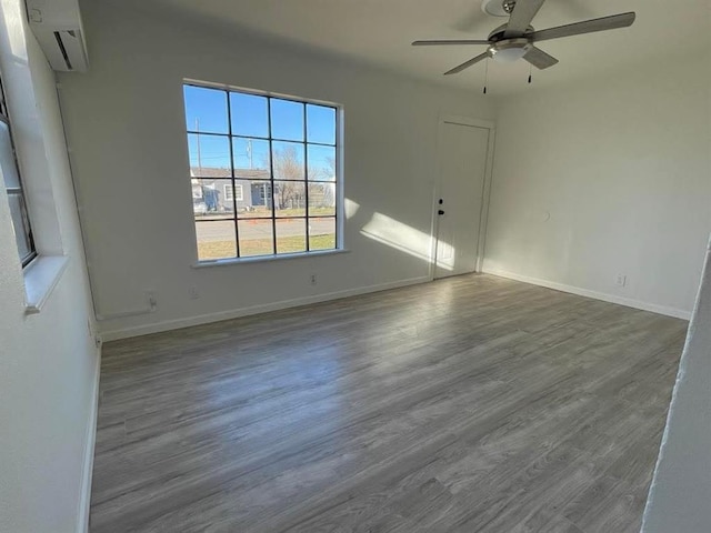 empty room with a wall unit AC, dark wood finished floors, baseboards, and ceiling fan