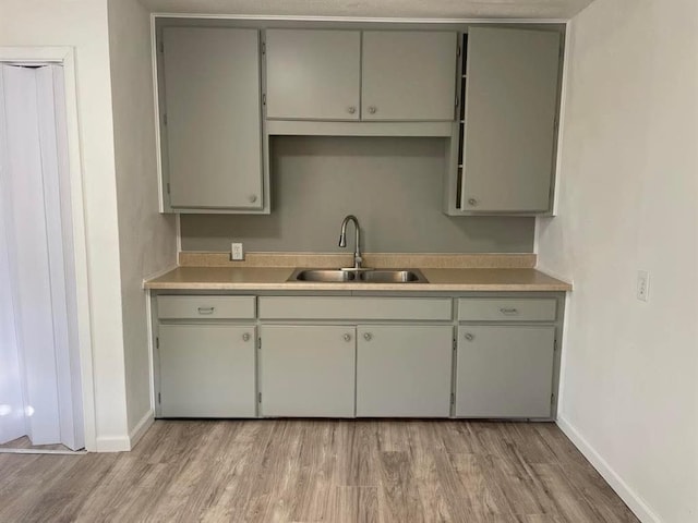 kitchen with light wood-style flooring, light countertops, a sink, and gray cabinetry