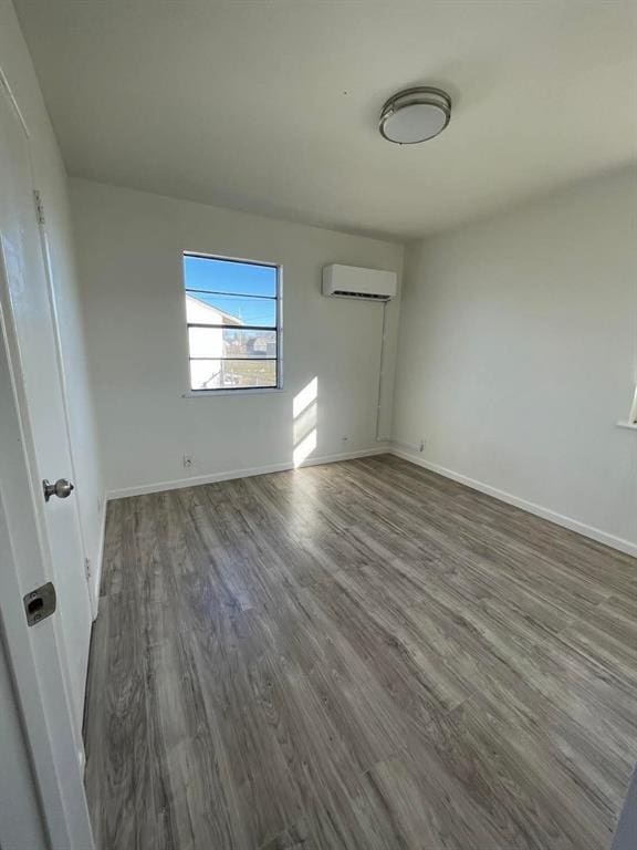 spare room with a wall unit AC, wood finished floors, and baseboards