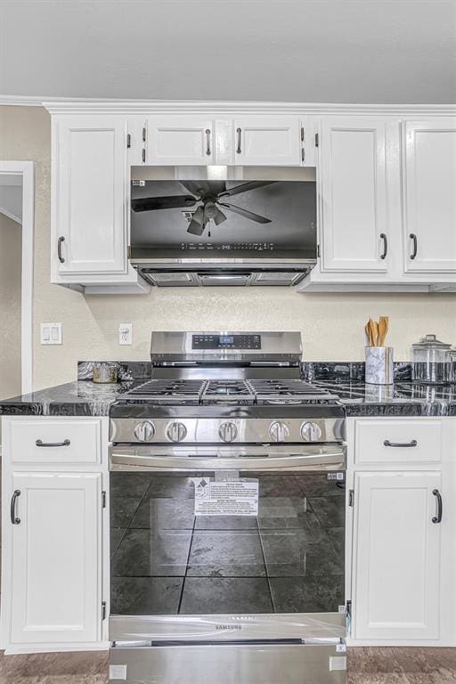 kitchen with ventilation hood, dark stone countertops, gas range, and white cabinetry