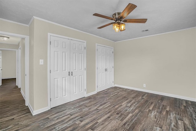 unfurnished bedroom with dark wood-type flooring, ornamental molding, and multiple closets