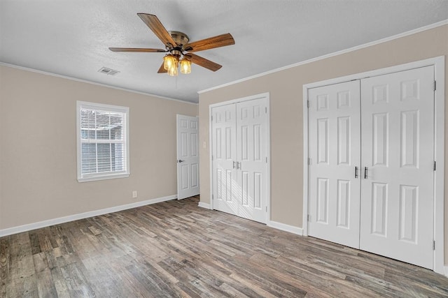 unfurnished bedroom featuring baseboards, visible vents, wood finished floors, crown molding, and multiple closets