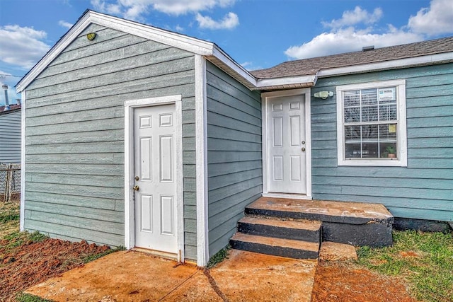 entrance to property featuring a shingled roof and fence