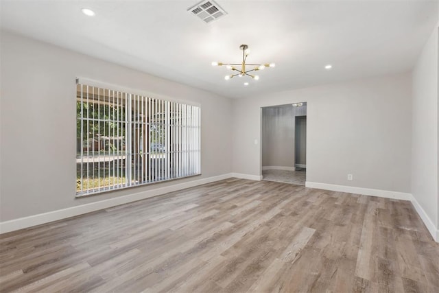 empty room featuring visible vents, a notable chandelier, baseboards, and wood finished floors