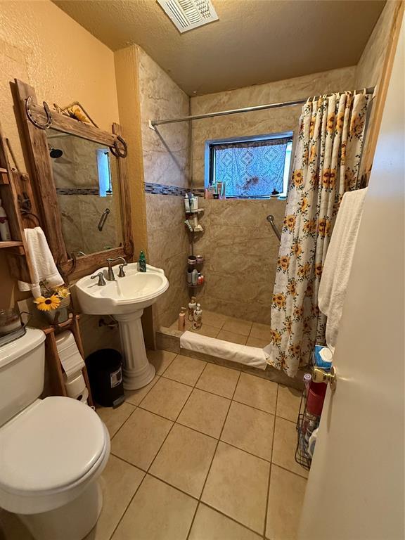 505 SE 18th St, Oklahoma City, OK 73129 - full bathroom with visible vents, toilet, a textured ceiling, tiled shower, and tile patterned floors