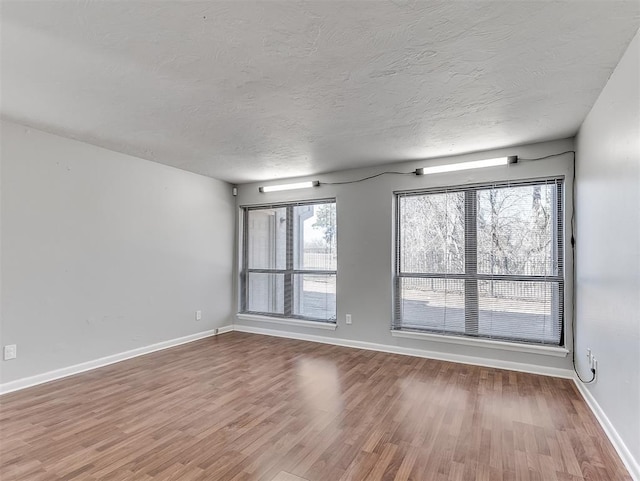 unfurnished room with a textured ceiling, baseboards, and wood finished floors