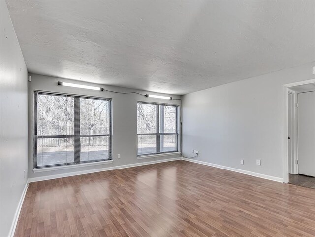 spare room featuring a textured ceiling, baseboards, and wood finished floors