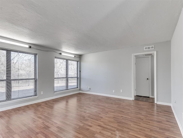 spare room featuring a textured ceiling, wood finished floors, visible vents, and baseboards