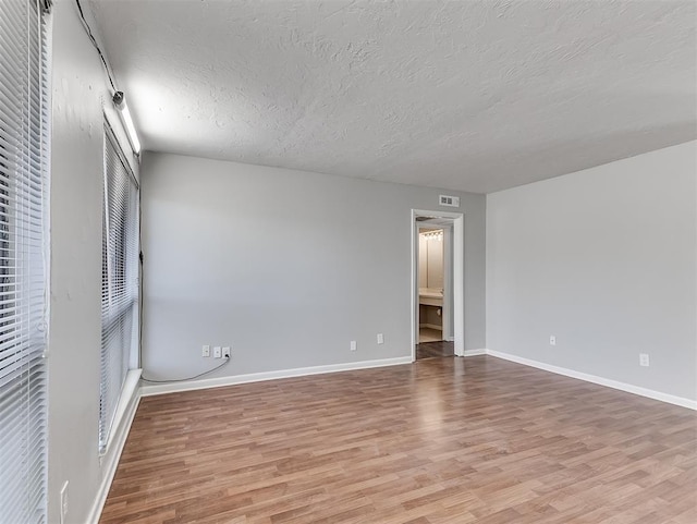 empty room with a textured ceiling, wood finished floors, visible vents, and baseboards