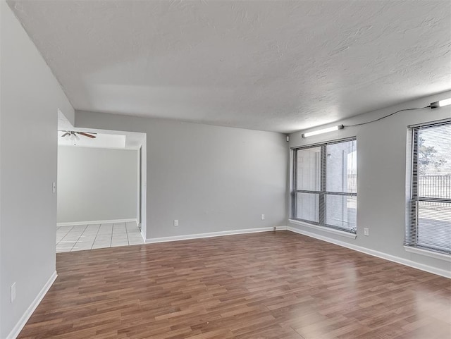 empty room with a ceiling fan, baseboards, a textured ceiling, and wood finished floors