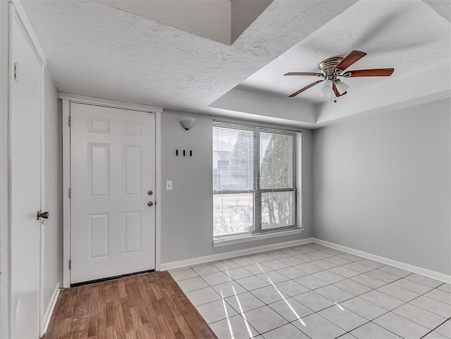 entryway featuring a textured ceiling, a ceiling fan, light wood-style floors, baseboards, and a tray ceiling