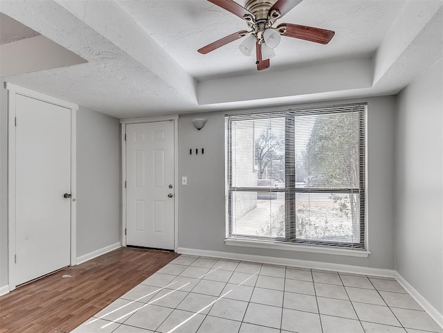 foyer entrance featuring light wood finished floors, ceiling fan, baseboards, and a textured ceiling