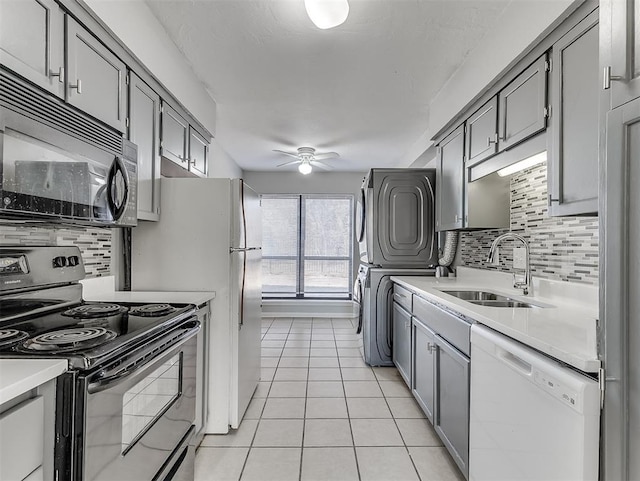 kitchen with light tile patterned floors, stacked washer and clothes dryer, gray cabinetry, black appliances, and a sink