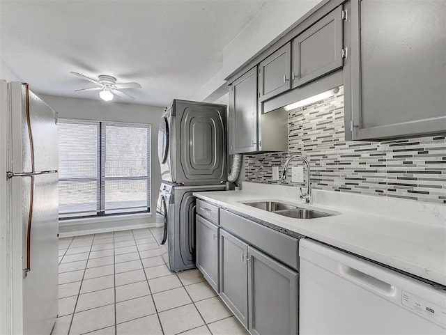 kitchen featuring stacked washer / drying machine, gray cabinets, backsplash, a sink, and white appliances