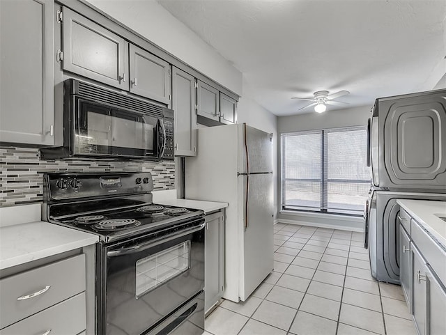 kitchen with stacked washer / drying machine, gray cabinetry, light countertops, and black appliances