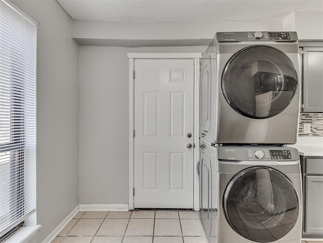 laundry area with baseboards, cabinet space, stacked washing maching and dryer, and light tile patterned floors