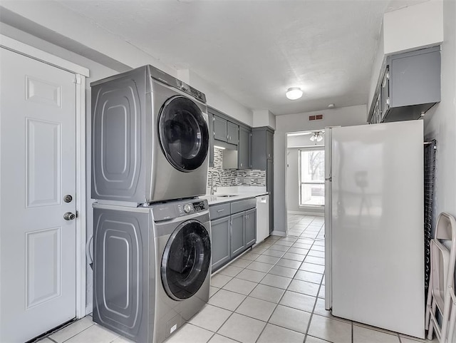 laundry room featuring stacked washer and clothes dryer, cabinet space, a sink, and light tile patterned floors