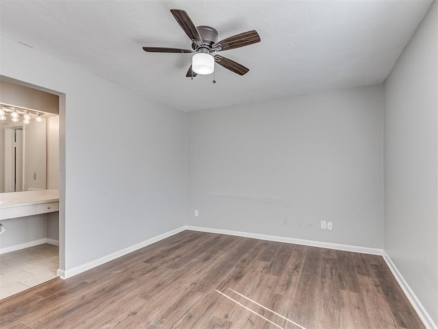 unfurnished bedroom featuring a ceiling fan, baseboards, wood finished floors, and ensuite bathroom