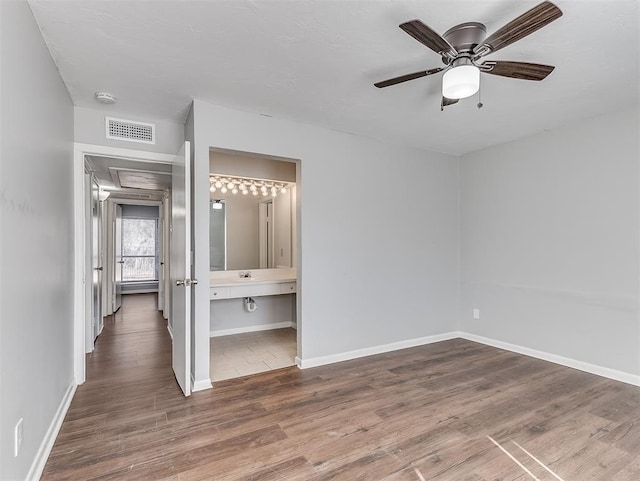 unfurnished bedroom with visible vents, ensuite bath, baseboards, and wood finished floors