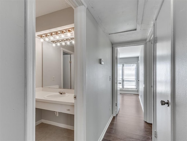 corridor featuring baseboards, a sink, and wood finished floors