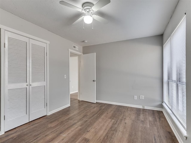 unfurnished bedroom with wood finished floors, a ceiling fan, visible vents, baseboards, and a closet