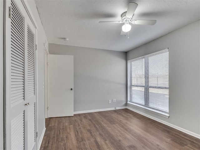 unfurnished bedroom featuring ceiling fan, a textured ceiling, wood finished floors, baseboards, and a closet