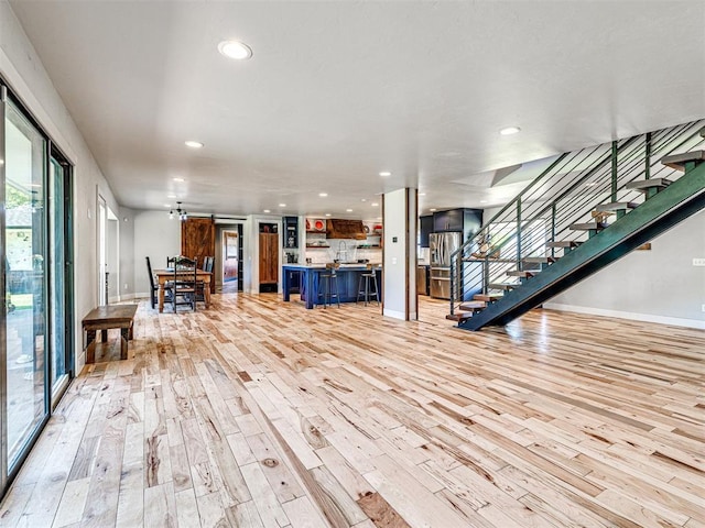 unfurnished living room featuring baseboards, stairway, recessed lighting, and light wood-style floors