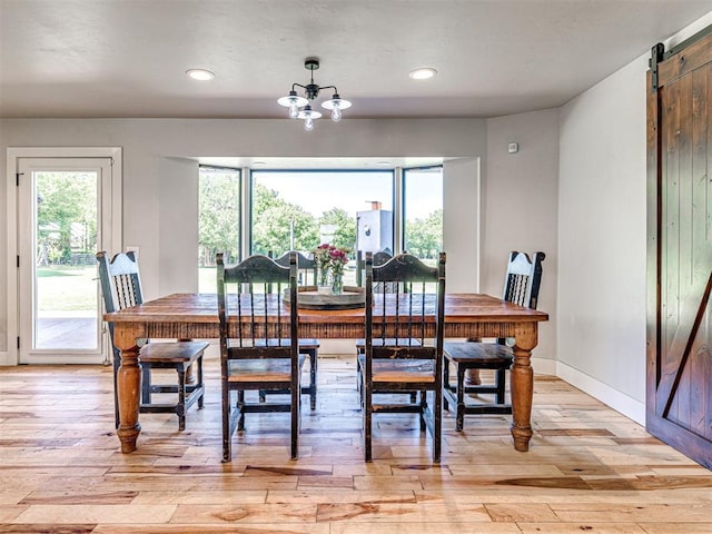 dining room featuring a healthy amount of sunlight, light wood finished floors, a barn door, and a chandelier