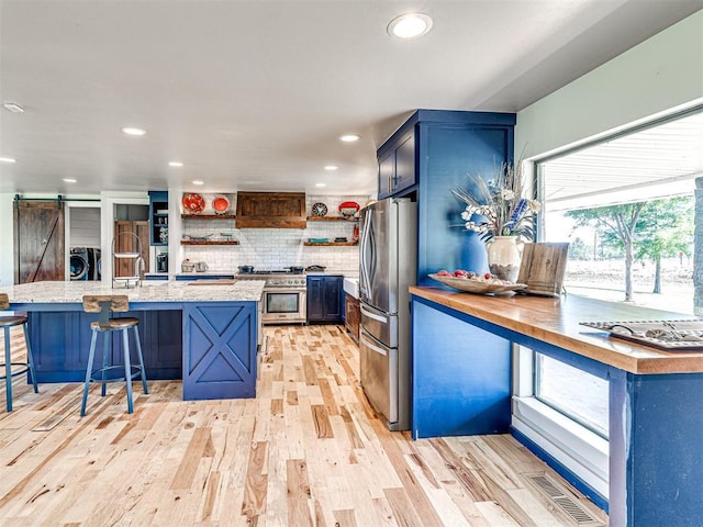 kitchen with a barn door, blue cabinets, visible vents, appliances with stainless steel finishes, and open shelves