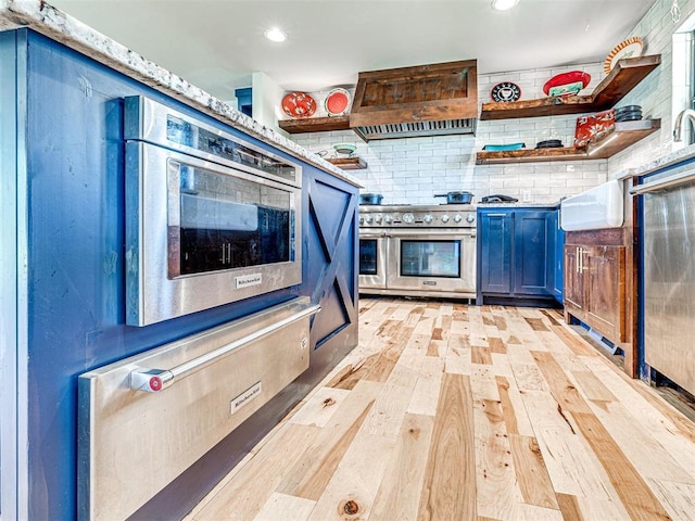 kitchen with light wood finished floors, custom exhaust hood, stainless steel appliances, blue cabinetry, and open shelves