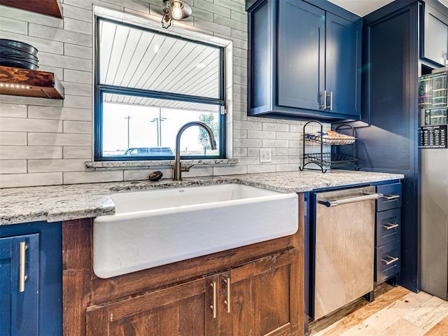 kitchen with light stone counters, a sink, stainless steel dishwasher, blue cabinetry, and backsplash