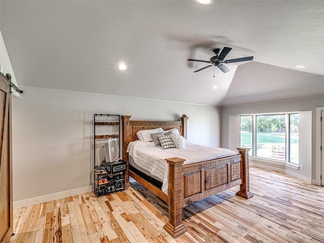 bedroom with ceiling fan, light wood-type flooring, vaulted ceiling, and a barn door