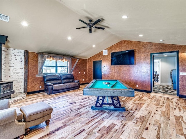 playroom with visible vents, a ceiling fan, vaulted ceiling, wood-type flooring, and a wood stove