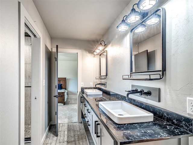 full bath featuring a textured wall, double vanity, a sink, and wood finished floors