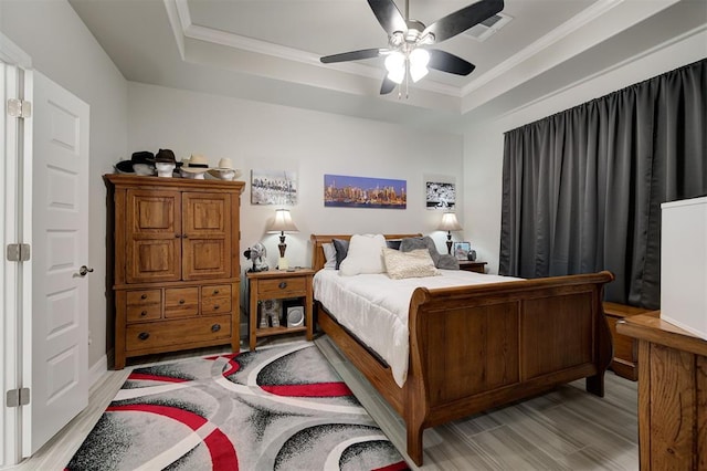 bedroom featuring ornamental molding, light wood-type flooring, a raised ceiling, and visible vents