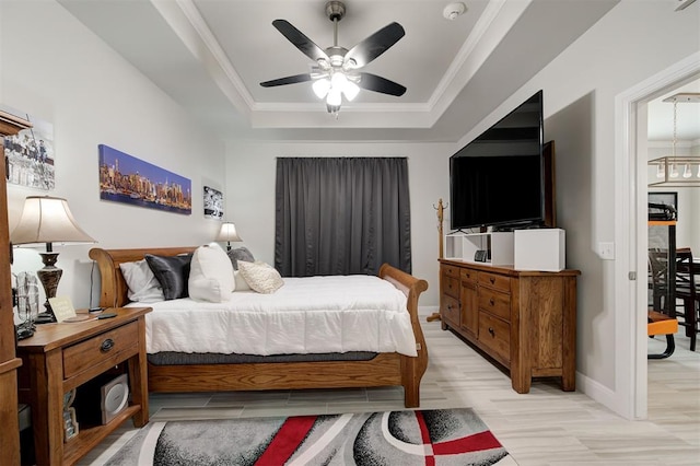 bedroom featuring baseboards, a raised ceiling, ceiling fan, ornamental molding, and light wood-type flooring