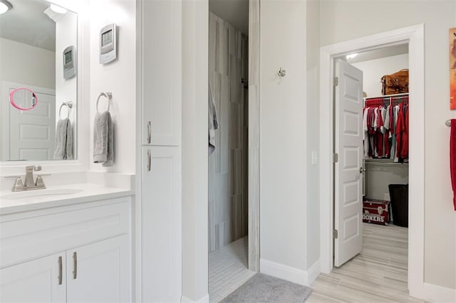 bathroom with a walk in shower, wood finished floors, a walk in closet, and vanity